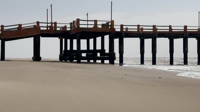 The ocean pier, sand beach below. Wooden jetty extending over low tide