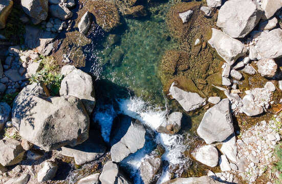 Aerial view of Rocky River with Pristine Waters Flowing Between Dense Forest Trees Covered with Moss and Vines in Indonesia. Serene Wilderness Landscape.