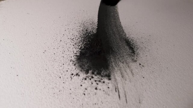 Watercolor graphite pigment spreading with a paintbrush across textured paper, flowing brush marks developing in slow motion