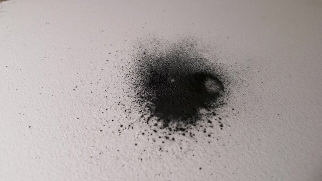 Watercolor graphite pigment dispersing across textured paper, creating irregular fluid patterns and tonal variations in slow motion