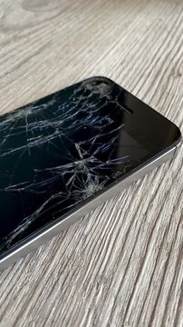 View of the broken phone screen. Cracked glass. A broken smartphone. Wooden background. Close up. 4k	