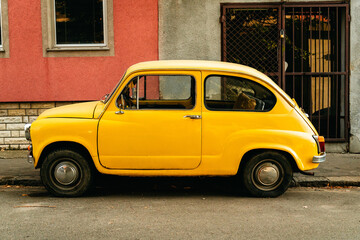 A vintage yellow compact car is parked on a street in Belgrade Serbia. The image suits classic transport nostalgia travel restoration and automotive themes. © Ekaterina