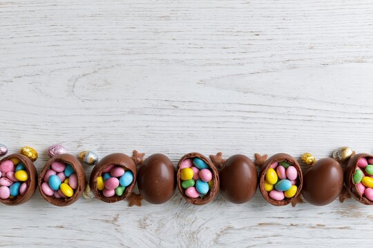 The Colorful Easter Chocolate Eggs Row with Candy Filled Halves on White Wood