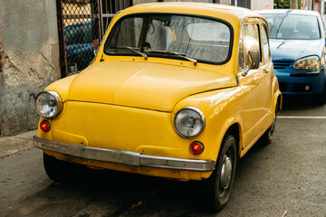A vintage yellow compact car is parked on a city street in Belgrade Serbia. The front view suits classic transport nostalgia restoration and automotive themes. © Ekaterina