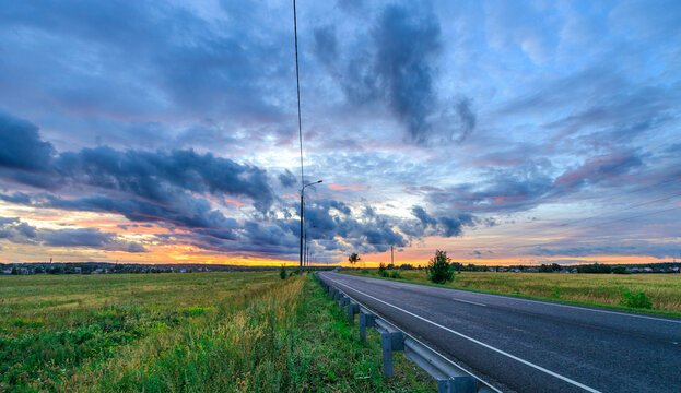 Empty highway under colorful sky with dramatic clouds at sunset
