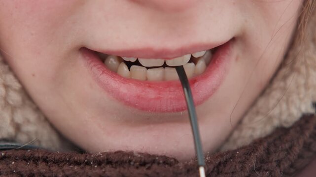 Tight frontal close view of lower face holding thin black cable between teeth, tugging downward with mouth, then easing into relaxed closed lips, highlighting skin texture, teeth, and subtle focused