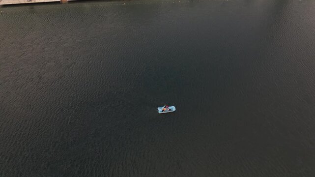 Aerial view of couple riding blue pedal boat on calm river water during sunset.