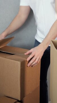 Mover's hands carefully folding and closing a brown cardboard box, preparing for shipping, moving house, or organizing storage in a new apartment after relocation or delivery