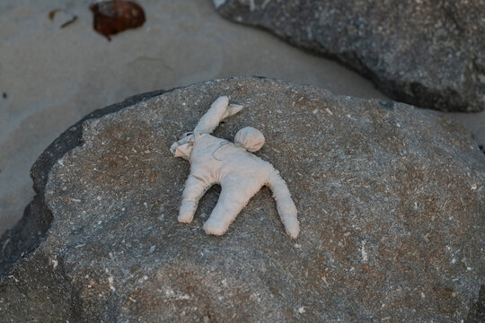 A discarded handmade cloth effigy used as a symbolic ritual object sits flat against a textured coastal rock on a beach in Maputo.