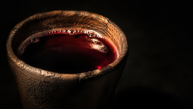 Red wine in ancient clay cup on black background. Miracle of Jesus turning water into wine at wedding in Cana of Galilee. Biblical story, Christian faith and holy communion concept