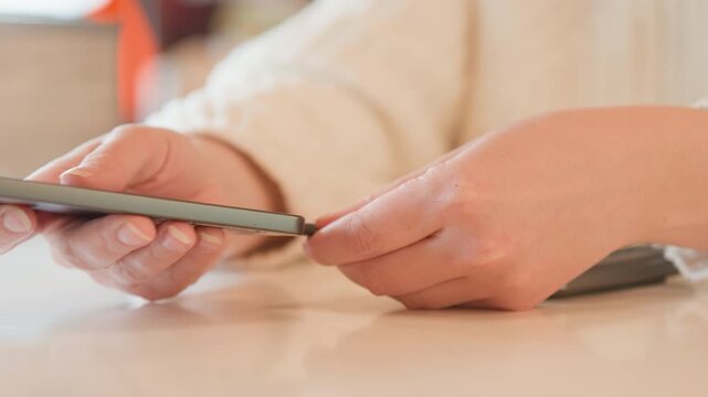 Close-up view of two mobile devices on tabletop with frayed charging cable linking ports, exposed inner wires, worn sheath, and hands guiding plug into place during careful troubleshooting