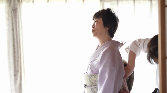 Side view of a woman in a lavender kimono as an assistant adjusts the obi at her back. Japan, April 19, 2025, spring.