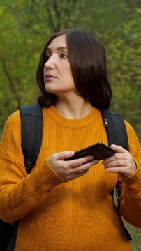 Worried female tourist with a backpack getting lost in the forest and trying to find a location using her smartphone. Brunette woman holding a mobile phone looking for a signal