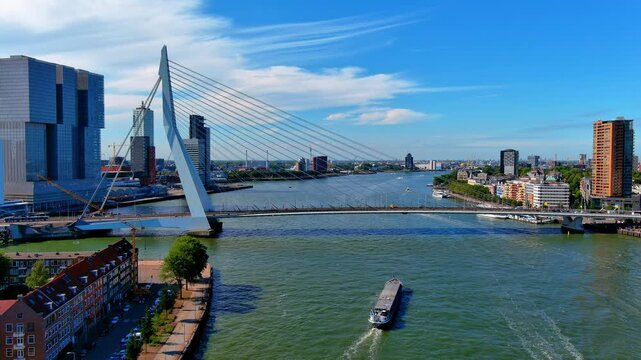 Aerial view of a cargo ship sailing under the Erasmus Bridge on the Nieuwe Maas river past Noordereiland, Rotterdam, Netherlands