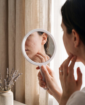 Woman checking her skin in a handheld mirror at home