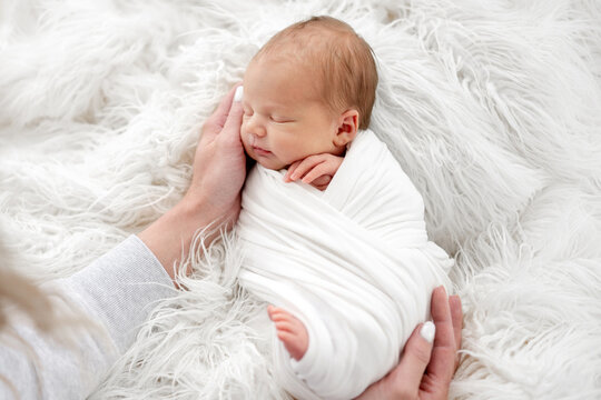 Parent cradles peaceful newborn child resting on fluffy white blanket indoors