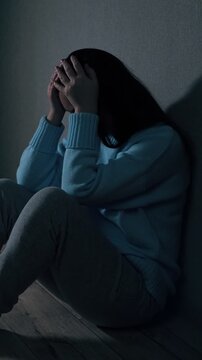 Sad and lonely young woman sitting on the floor in a dark empty room, covering her face with her hands, feeling hopeless and depressed while experiencing emotional problems and solitude