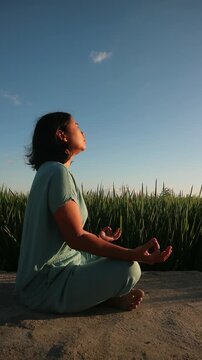 Young woman meditating in a green field during a peaceful golden hour sunset. outdoor wellness activity