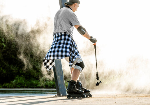 Man wearing protective gear records video while rollerblading on a dusty outdoor track at sunset