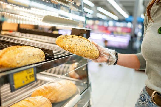 Shopper wearing plastic glove picks fresh bread from supermarket shelf during daytime shopping trip