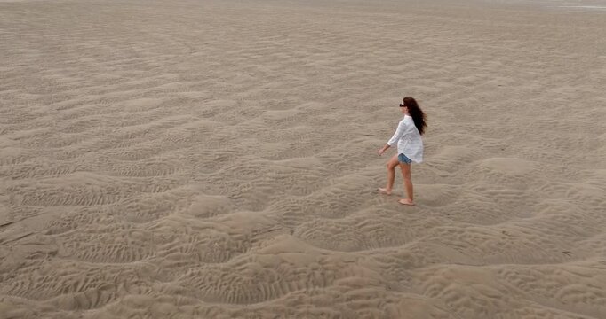 Caucasian long hair woman walking barefoot across wide, textured sandy beach in Ko Lanta, Thailand, highlighting concepts of freedom, exploration, and solitude in natural landscape, travel and explore