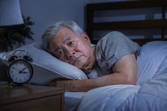 An elderly man struggles to sleep, reflecting a moment of insomnia and deep thought in a dimly lit room.