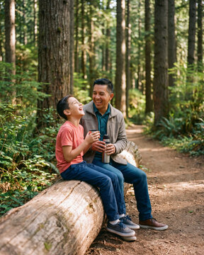 Reflective father and son sitting on fallen log along forest trail with warm natural light