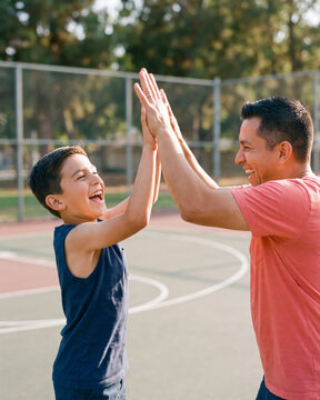 Spirited father and son sharing a high five on sunny basketball court with warm natural light