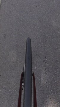 Vertical POV footage showing a cyclist and bicycle shadow moving across an asphalt road, capturing outdoor cycling, active lifestyle and a unique first person riding perspective.