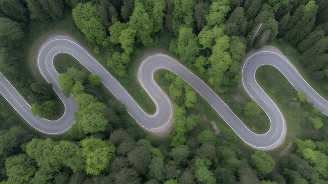 Down aerial view of a winding asphalt road snaking through a lush green forest with sharp hairpin turn curves seen.