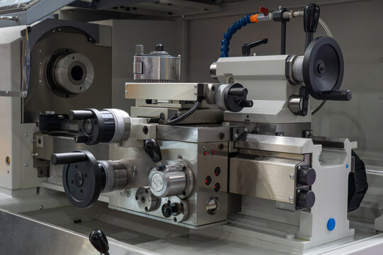 Close-up of metal lathe machine apron, carriage, tool post, and handwheels in industrial manufacturing workshop