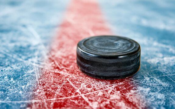 Black hockey puck on red line of ice rink close up