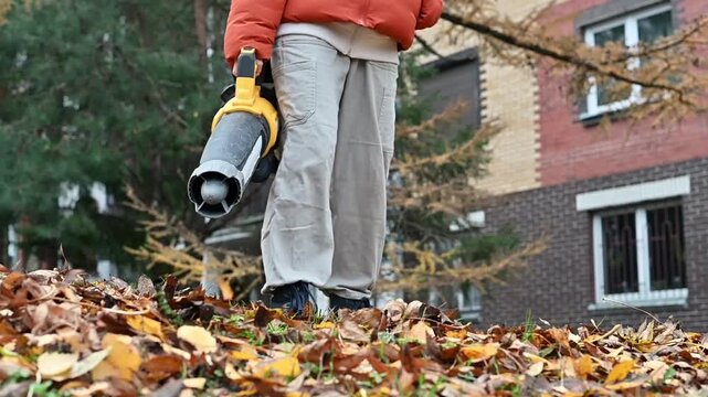 Teenage girl using a leaf blower to clear fallen leaves in autumn. Seasonal yard and garden cleanup, outdoor work, property maintenance, and fall home care.