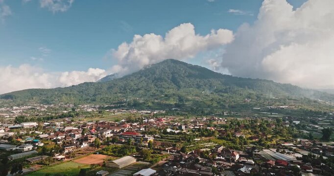 Mount Agung volcano rising above a village surrounded by green fields in Bali, Indonesia. Aerial view drone flight panorama