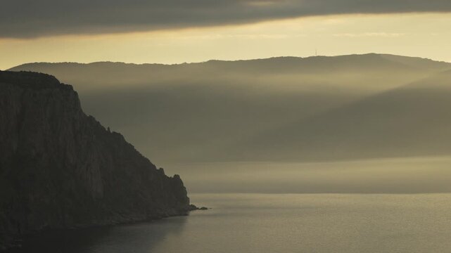Mountain fog sunbeams coastal mountain range shrouded in morning fog with sunbeams piercing through clouds over a calm sea at sunrise