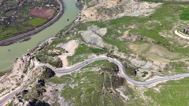 Smooth 4K aerial flight over a mountain road, winding river and historic ruins, moving gently forward and right to reveal the surrounding green spring landscape.