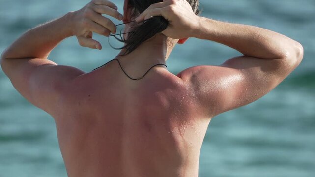 Sunburned man tying wet hair back at the ocean beach