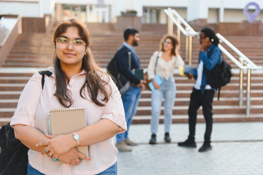 Smiling indian student holding books on campus