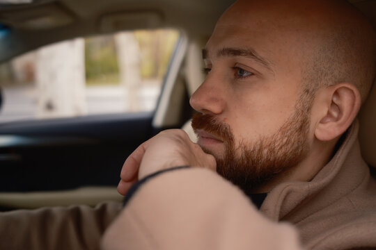 Man in beige coat sitting inside a car looking thoughtful and composed