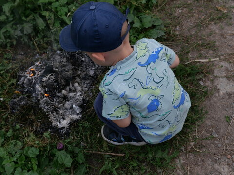 Little boy in a cap looking at a dying bonfire outdoors
