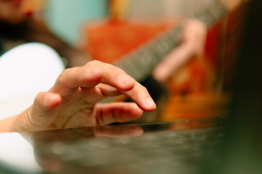 Close-up of hand on laptop trackpad with blurred electric guitar background during online music lesson.
