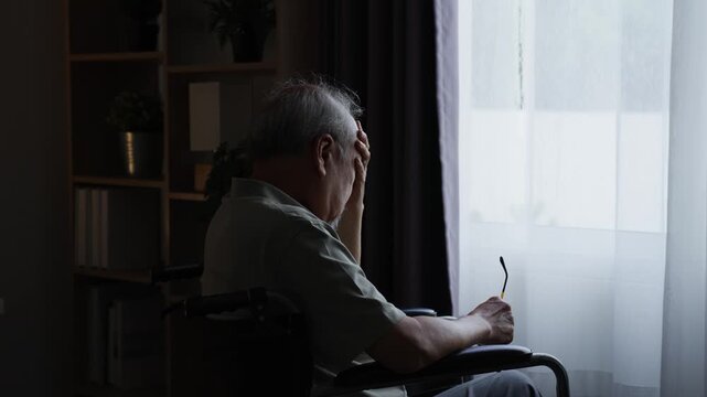 Senior man raising his hand and gesturing while sitting in wheelchair near window.