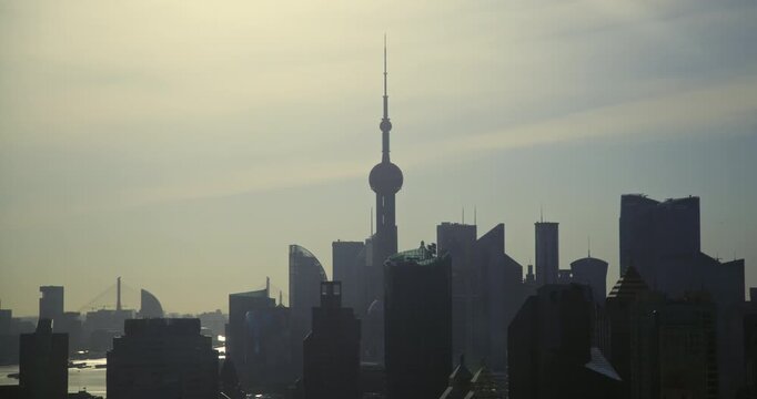 Dark silhouettes of Oriental Pearl Tower and Pudong skyscrapers stand against an orange dawn sky brightening into daylight over Shanghai, recorded in timelapse