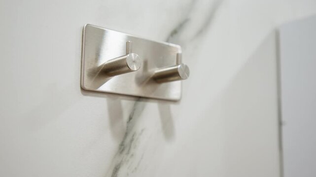 Chrome double hook on veined marble wall, revealing empty polished mount with reflective metal, subtle shadow, and clean modern interior texture in close low-angle view, with hook, chrome, marble