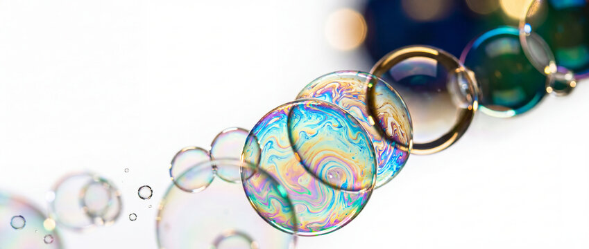 Soap bubbles with iridescent rainbow film patterns float diagonally across a bright white background with soft bokeh lights, creating a clean vibrant banner for scientific or creative design