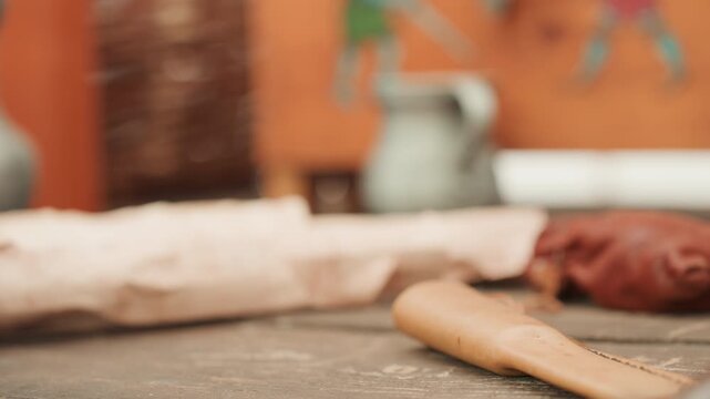 Low-angle close view of wooden spoon lying on worn sawdust-covered workbench with blurred log, knife handle, and assorted tools behind it, under warm indoor light for calm rustic atmosphere