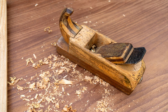 Old wooden hand plane with shavings on workbench. Vintage carpentry tool for woodworking and craftsmanship. Traditional joinery instrument concept for artisan workshop and handmade furniture making