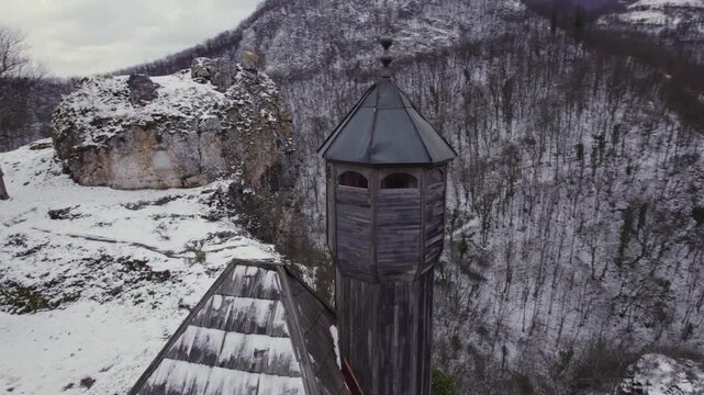 Aerial view of medieval wooden watchtower on snowy mountain cliff in winter.