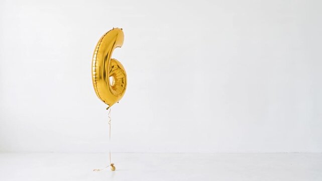 Large gold number six helium balloon floating against a clean white background with generous copy space, ideal for sixth birthday, anniversary, milestone and celebration concepts.
