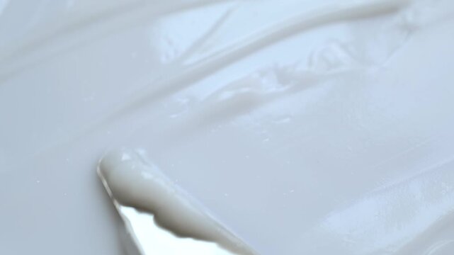 Close-up of spatula spreading smooth white cosmetic cream, showing its texture